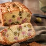 Cake jambon olive moelleux tranché sur une planche en bois, avec des olives vertes et du gruyère râpé visibles