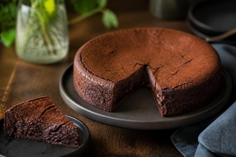 Gâteau au chocolat moelleux tranché sur une planche en bois, texture fondante visible, saupoudré de cacao, lumière naturelle douce